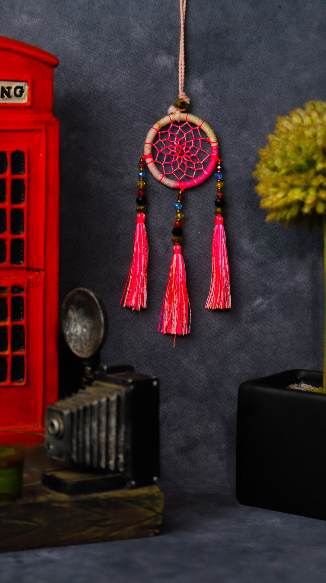 Mini dream-catcher tassel charm in rainbow tones hanging on a rear-view mirror.