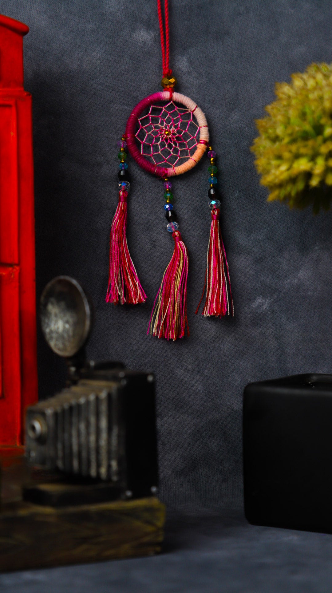 Mini dream-catcher tassel charm in rainbow tones hanging on a rear-view mirror.