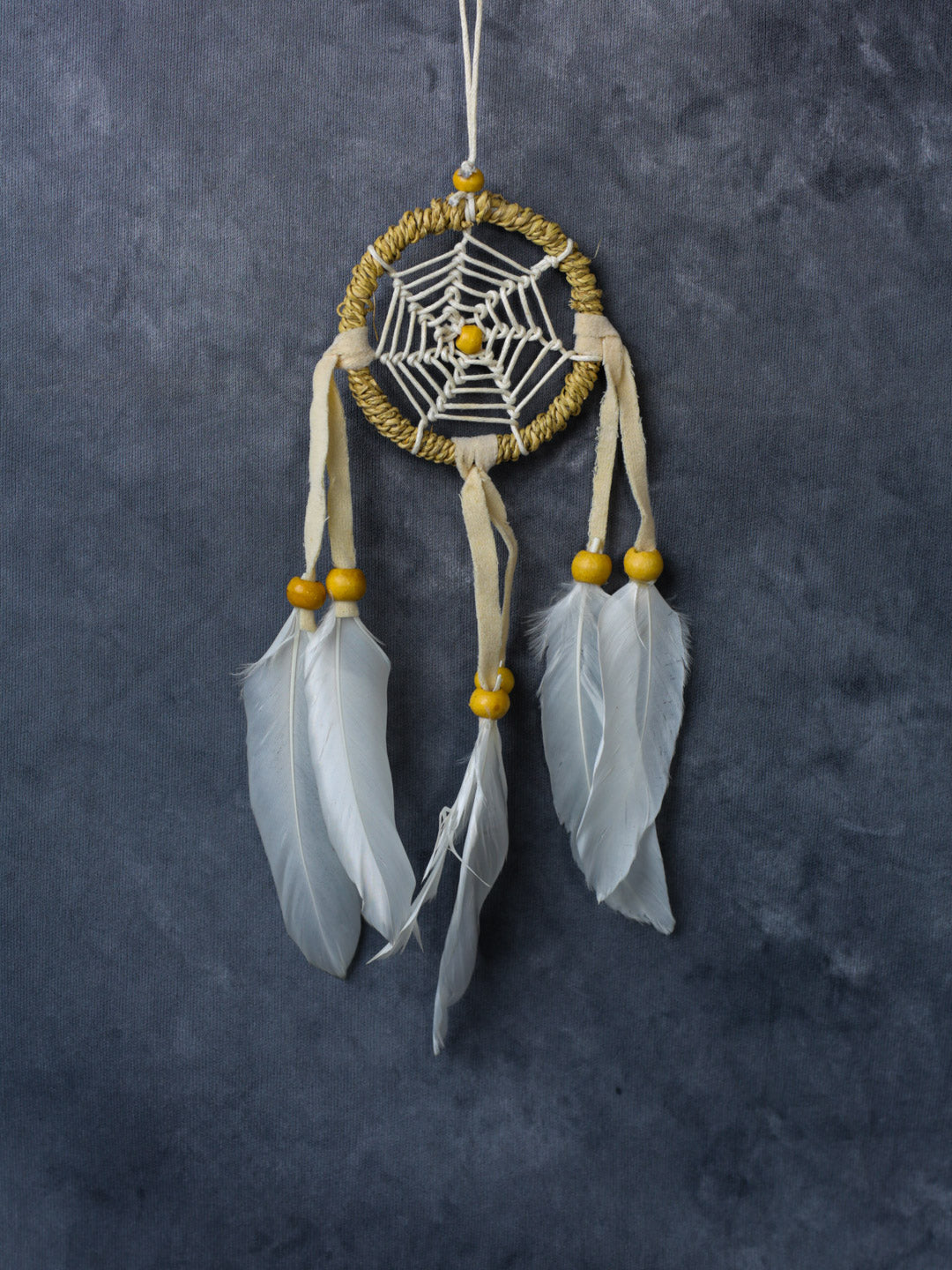 Hand-crafted cotton dreamcatcher with suede ties, wood beads and colorful feathers, sized for wall or car décor.