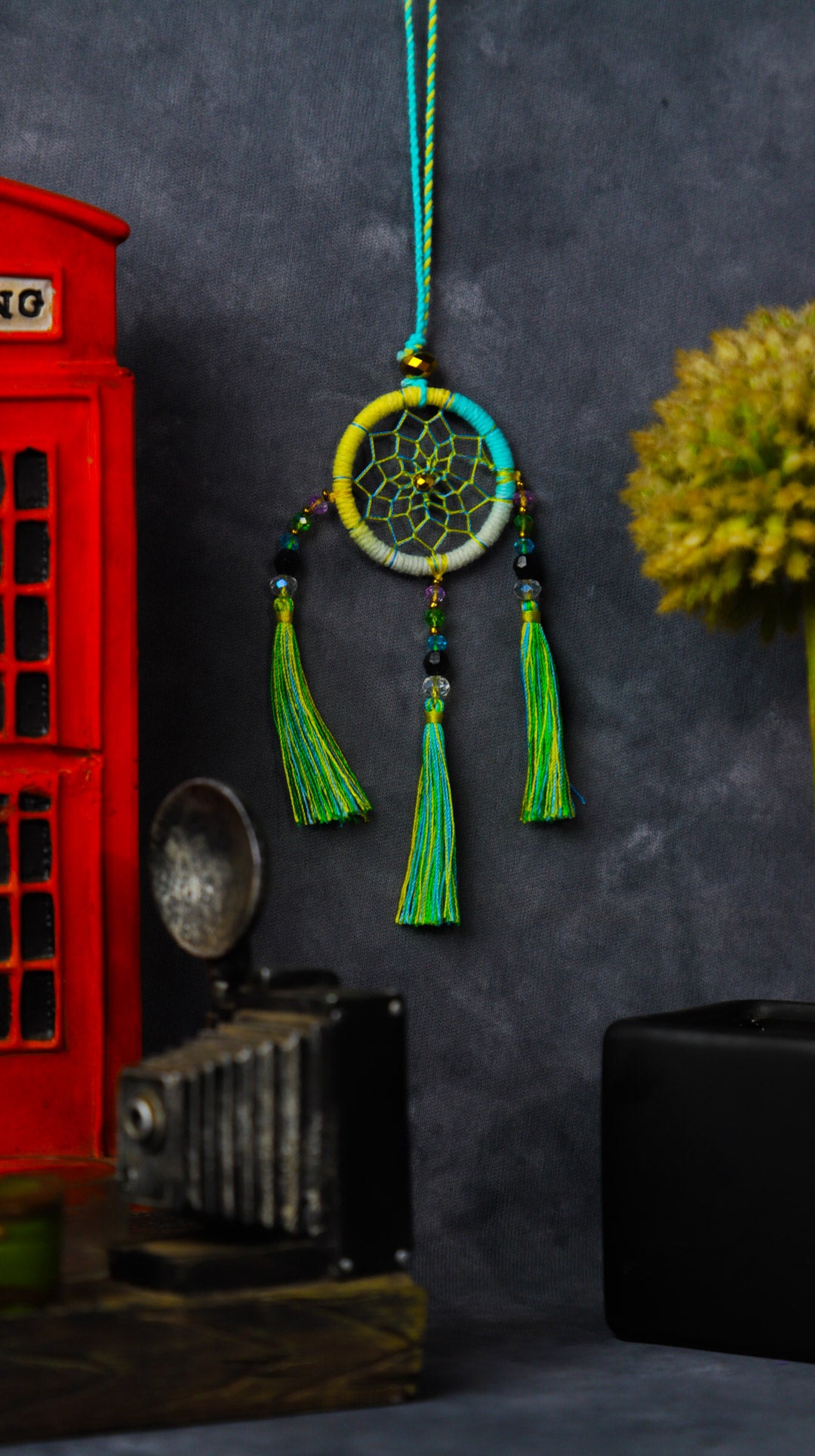 Mini dream-catcher tassel charm in rainbow tones hanging on a rear-view mirror.
