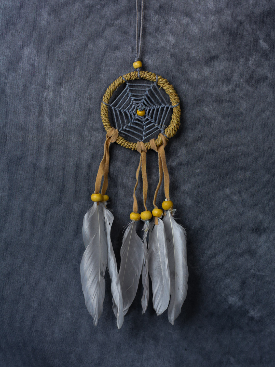 Hand-crafted cotton dreamcatcher with suede ties, wood beads and colorful feathers, sized for wall or car décor.