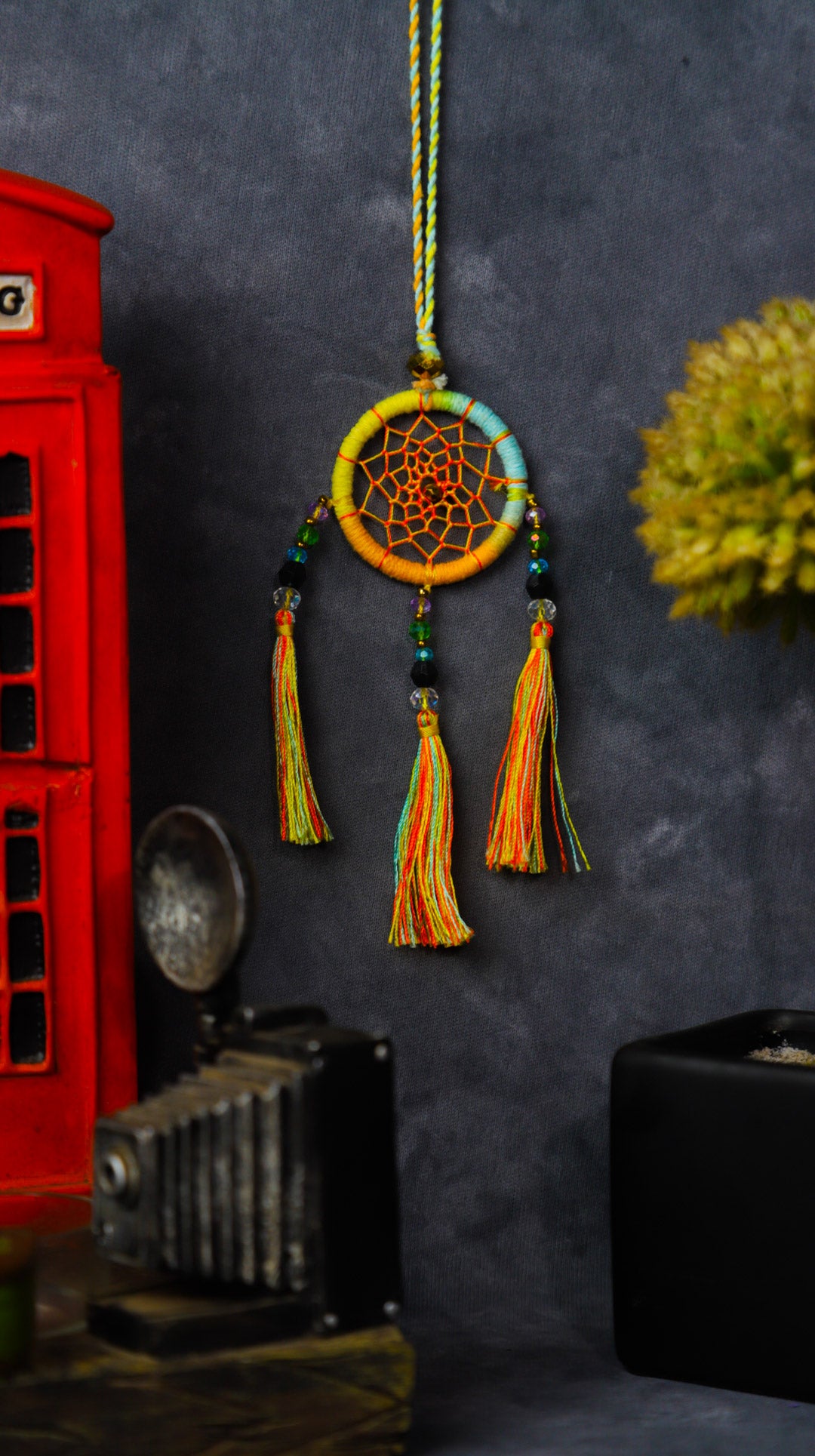 Mini dream-catcher tassel charm in rainbow tones hanging on a rear-view mirror.