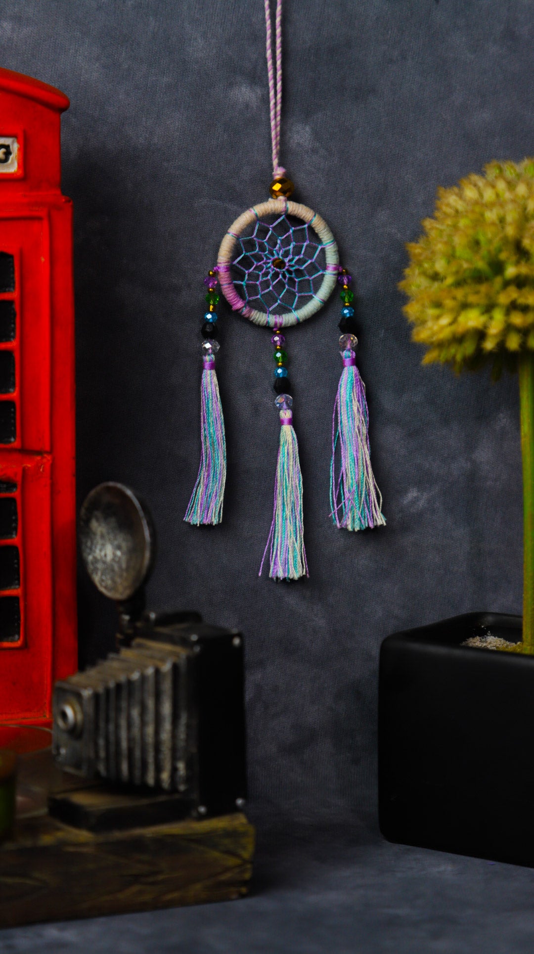 Mini dream-catcher tassel charm in rainbow tones hanging on a rear-view mirror.