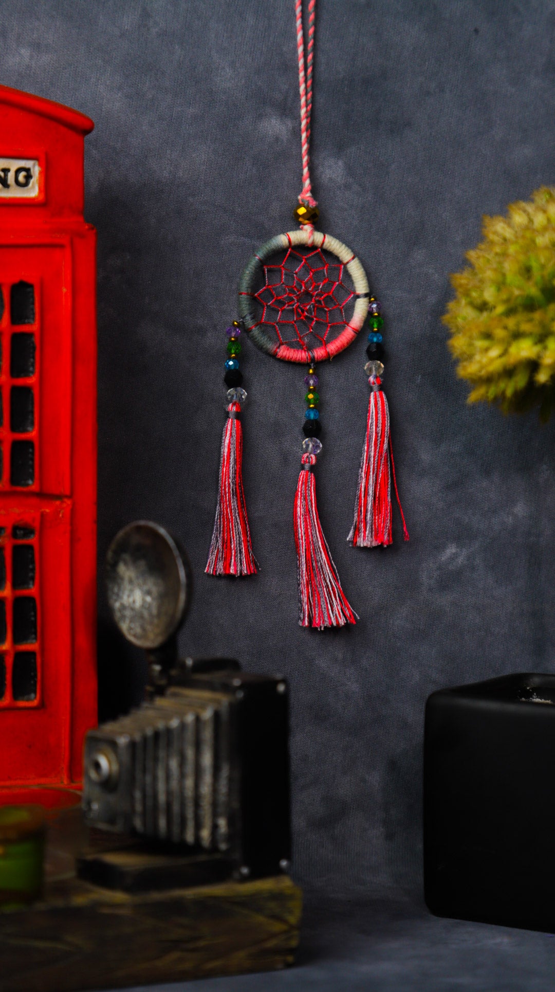 Mini dream-catcher tassel charm in rainbow tones hanging on a rear-view mirror.