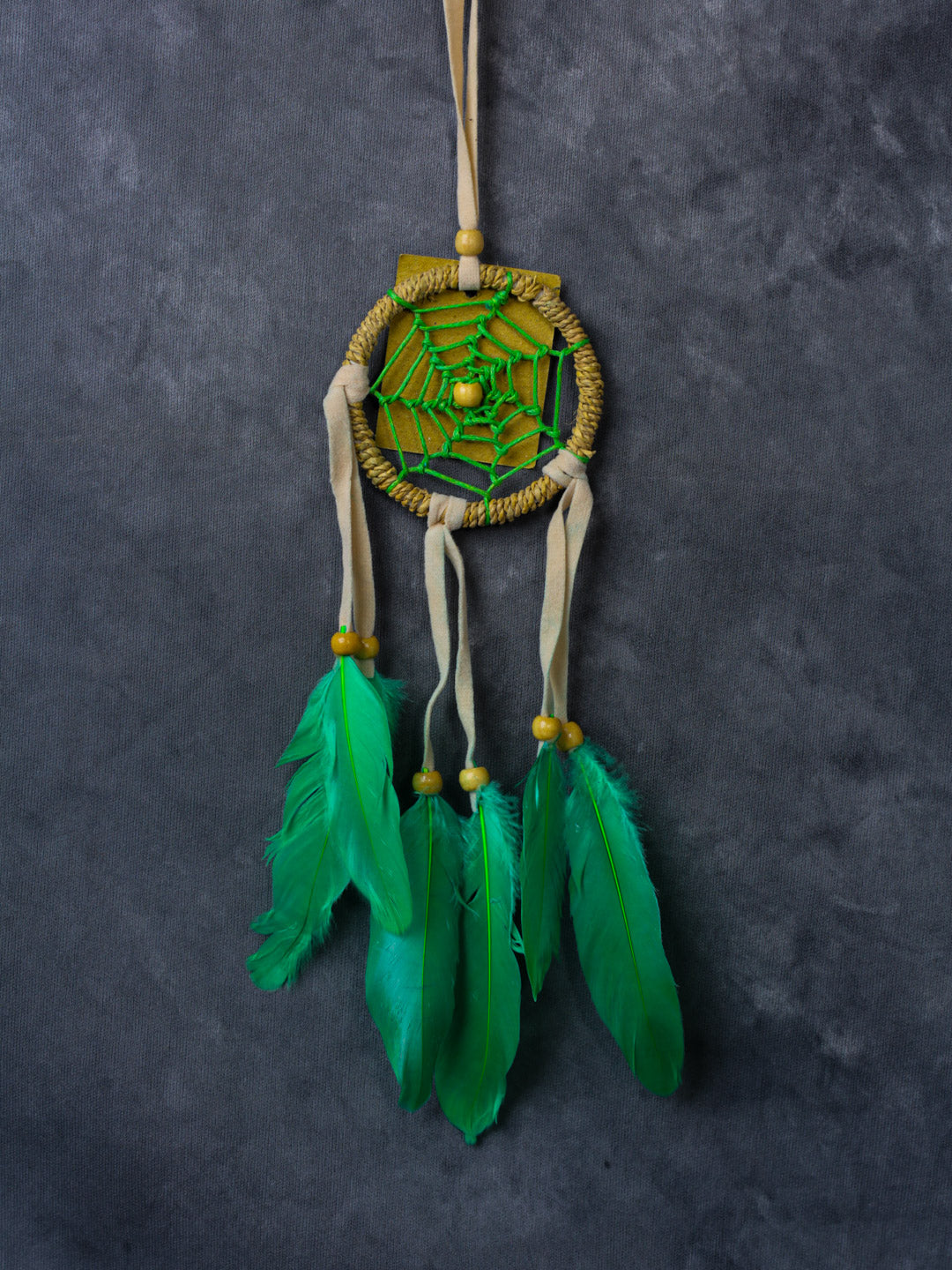Hand-crafted cotton dreamcatcher with suede ties, wood beads and colorful feathers, sized for wall or car décor.
