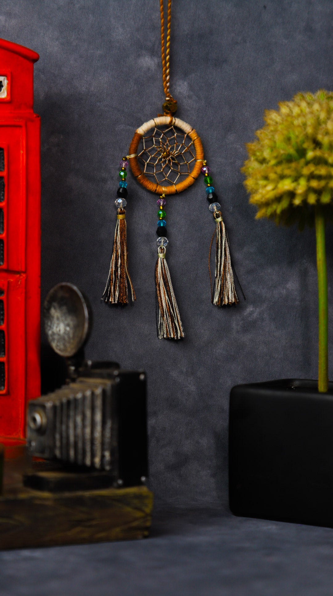 Mini dream-catcher tassel charm in rainbow tones hanging on a rear-view mirror.