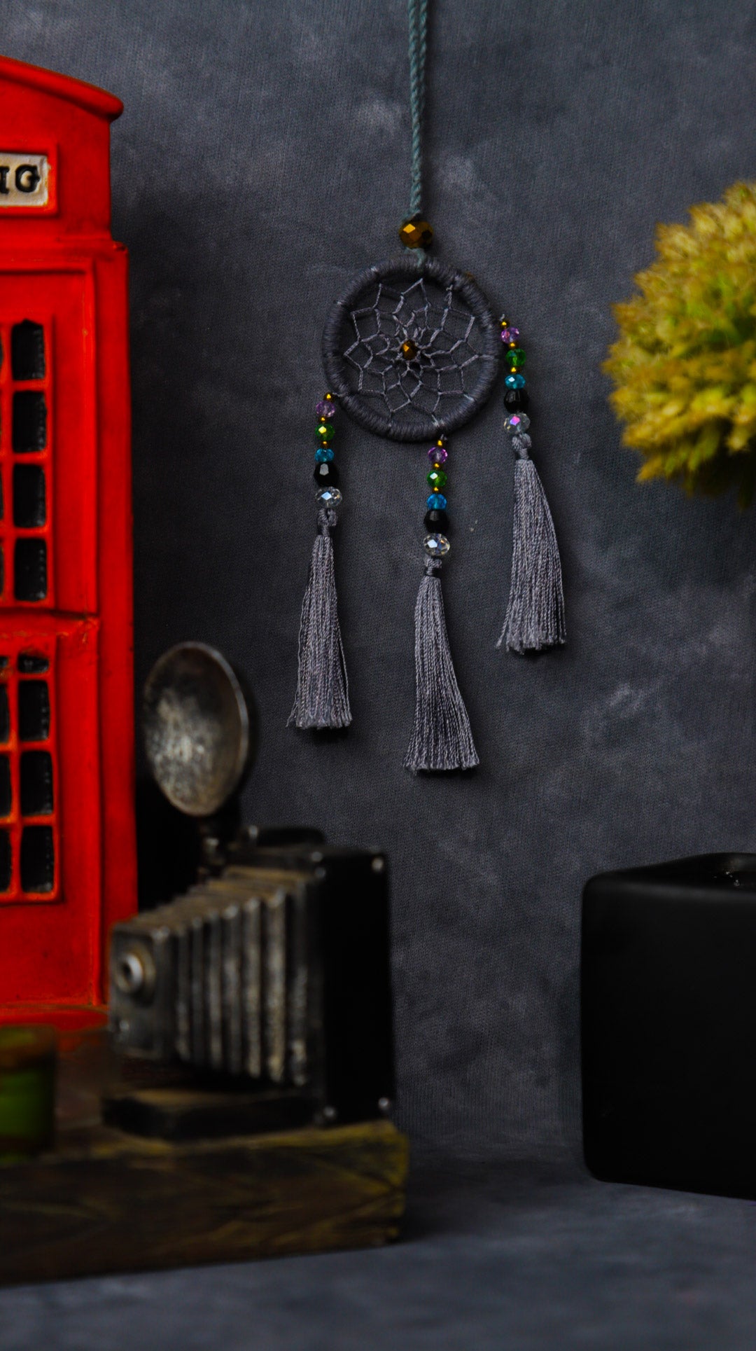 Mini dream-catcher tassel charm in rainbow tones hanging on a rear-view mirror.