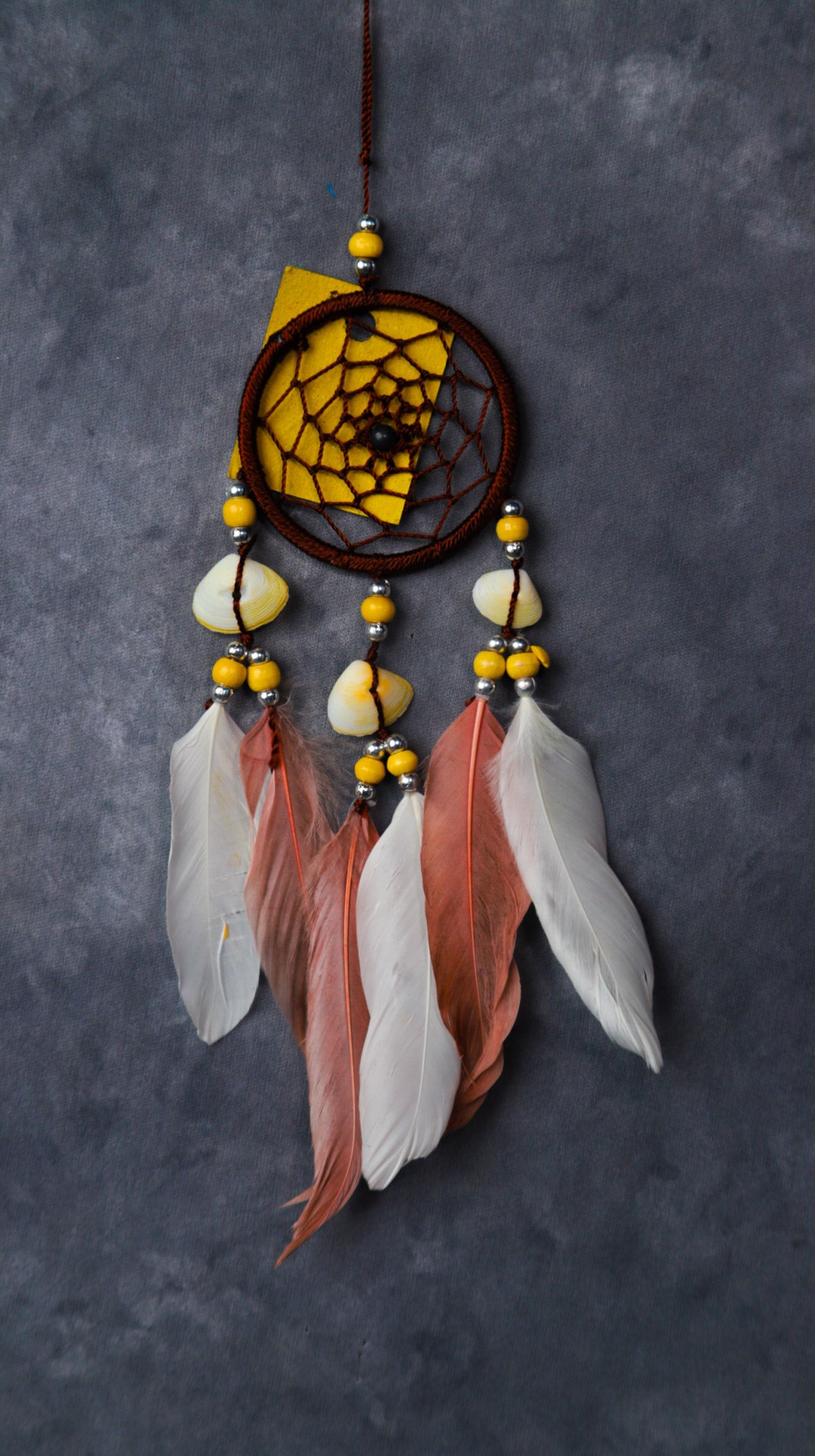 Close-up of a blue nylon dream-catcher with white and blue feathers hanging from a rear-view mirror.
