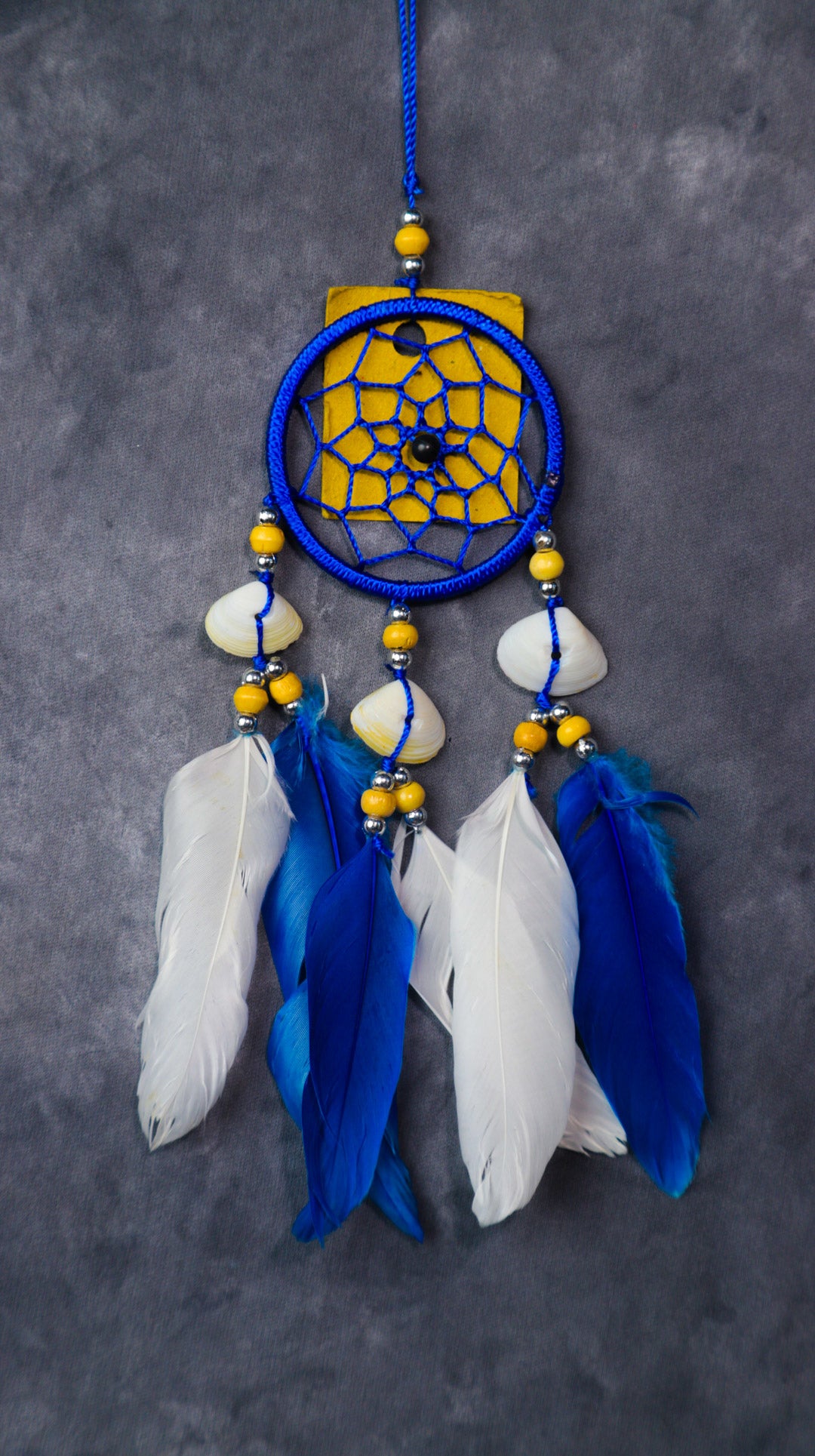 Close-up of a blue nylon dream-catcher with white and blue feathers hanging from a rear-view mirror.