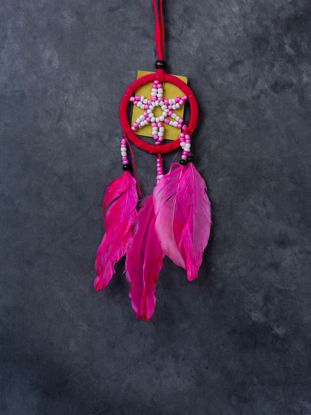 Pink beaded star dreamcatcher with three feathers, hanging ribbon, and cotton hoop.