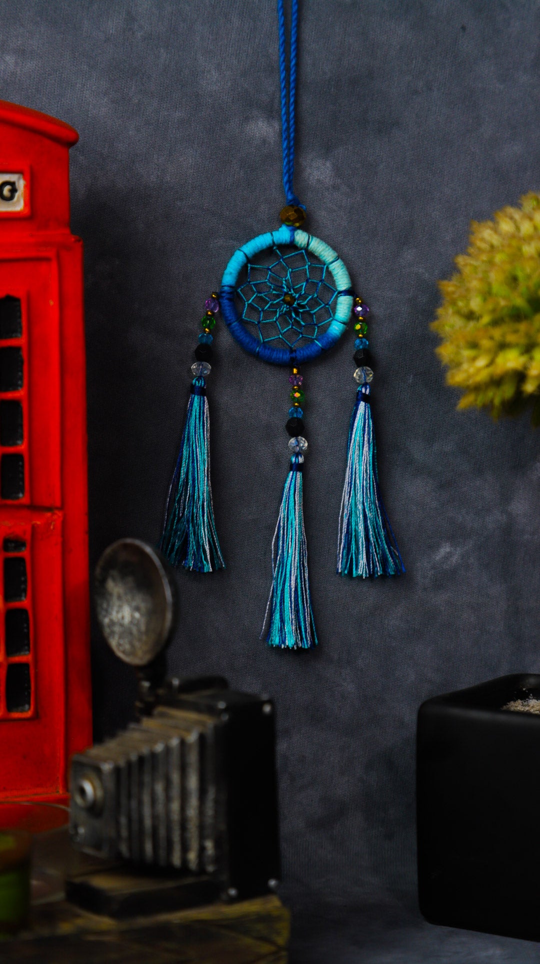Mini dream-catcher tassel charm in rainbow tones hanging on a rear-view mirror.